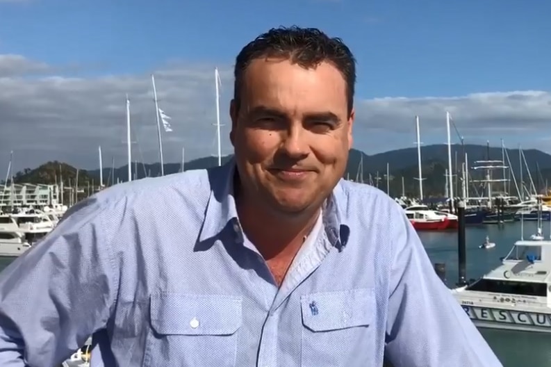 A man in a blue shirt smiling at a marina