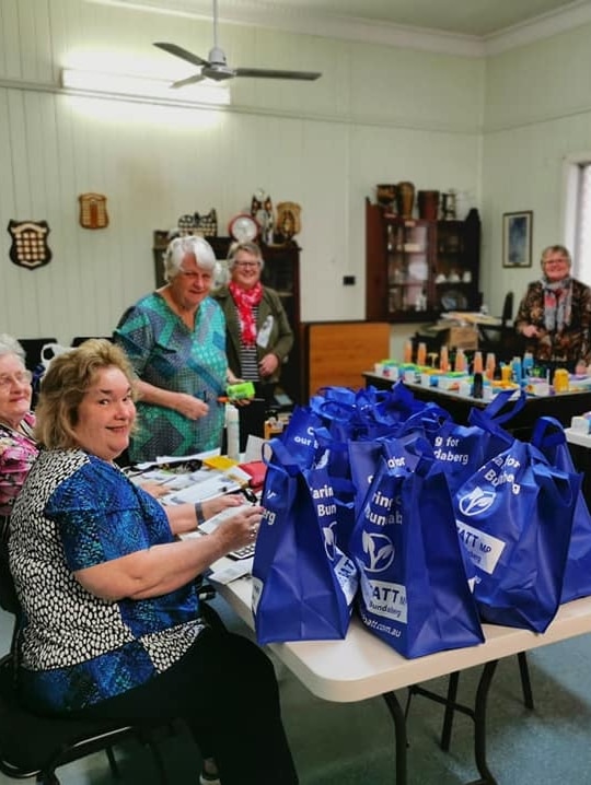 Six ladies in a room with a table stacked with reuseable bags and toiletry items.