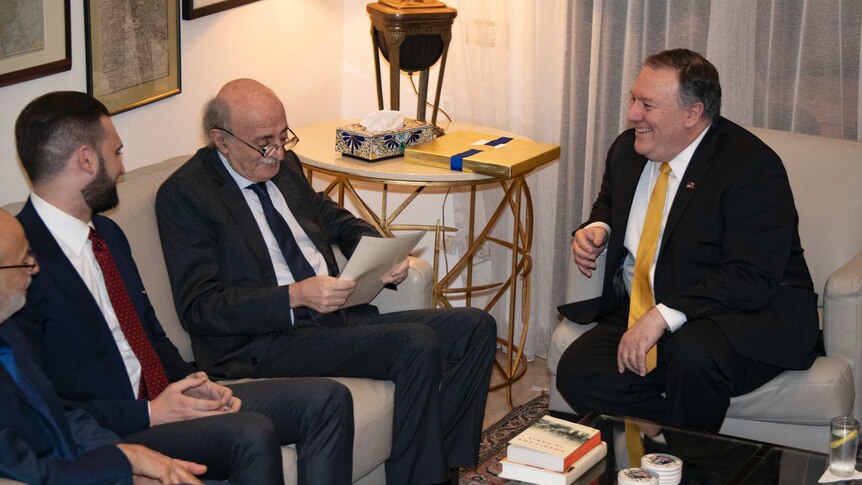 Walid Jumblatt, left, wearing glasses reads a document. To his right, Mike Pompeo is smiling. They are sitting on couches.