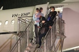 Passengers with their faces blurred disembark a plane at night.