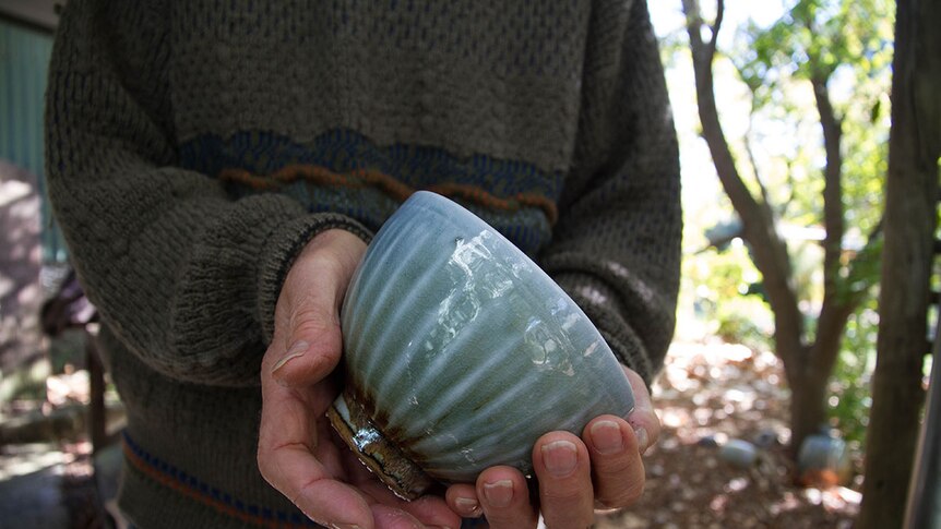 Man's hands hold a a green glazed bowl towards the camera.
