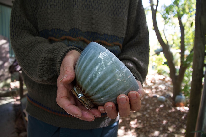 Man's hands hold a a green glazed bowl towards the camera.