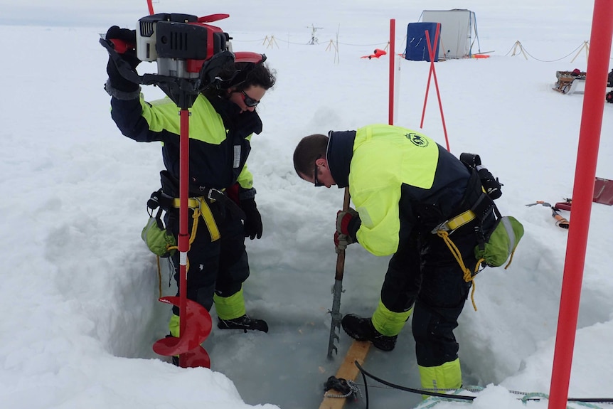 two people drilling through ice.