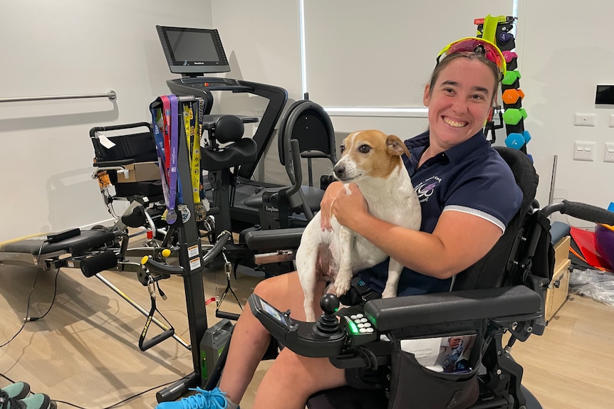 a woman in a wheelchair with a dog on her lap in a room full of exercise equipment