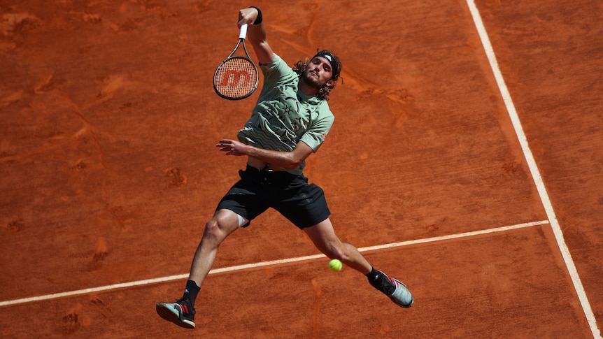 A tall tennis player points his racquet head down after hitting an overhead shot in mid-air during a match.