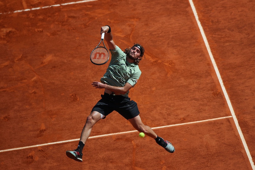 A tall tennis player points his racquet head down after hitting an overhead shot in mid-air during a match.