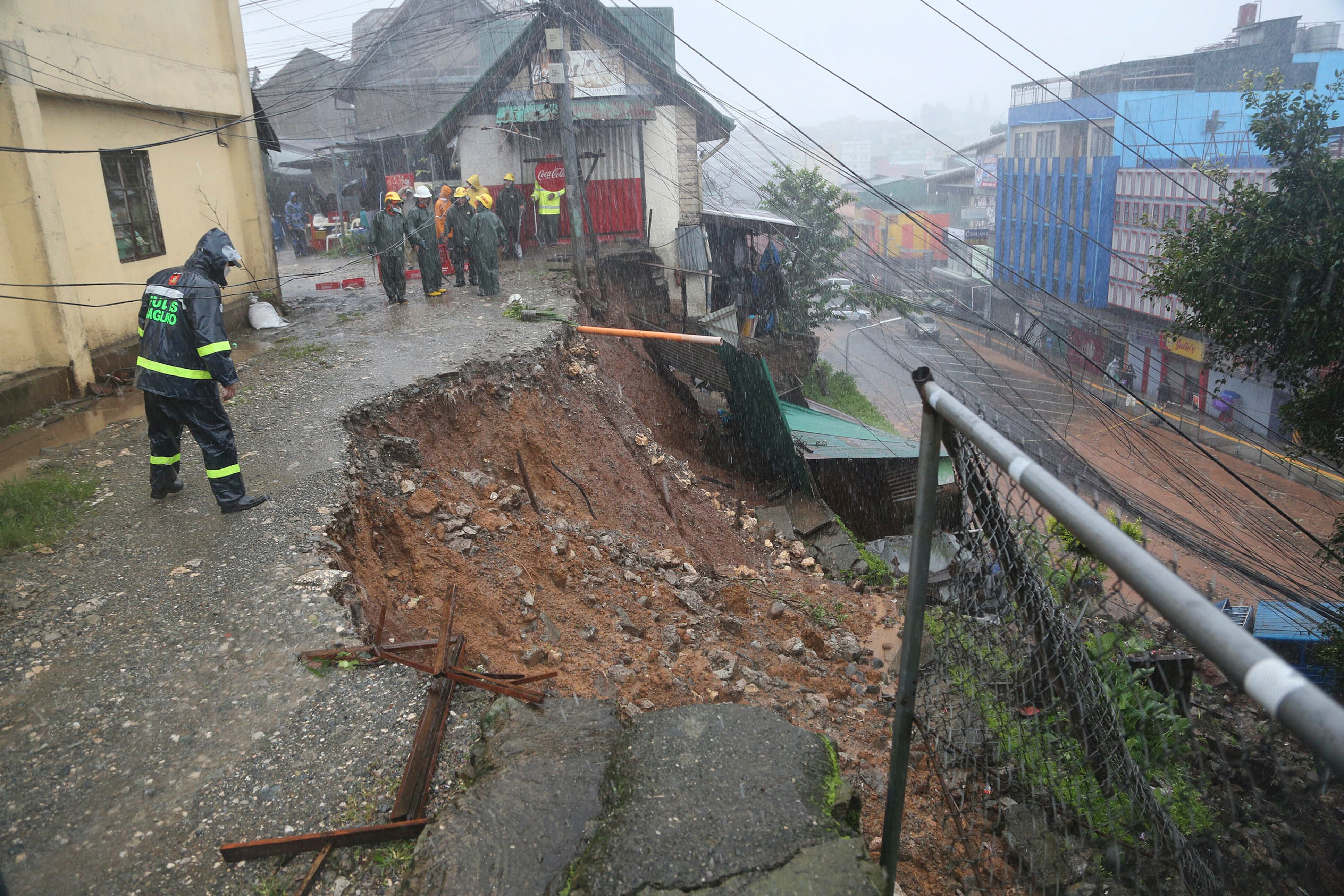 A police officer looks down on a landslide that has caved in the side of a road on top of houses.