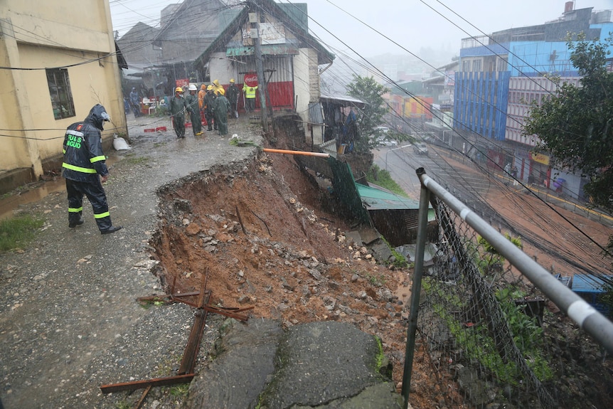 A police officer looks down on a landslide that has caved in the side of a road on top of houses.