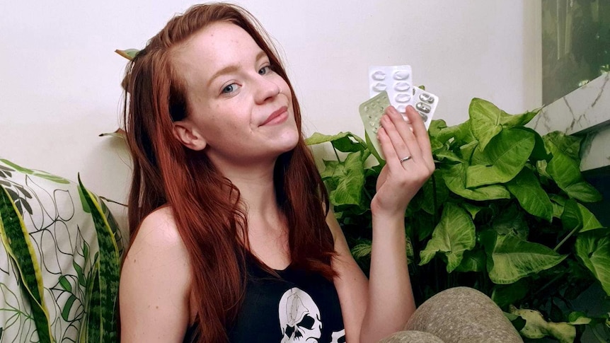 Kaitlyn Gillies sits in front of a house plant holding empty medication packaging, for a story about reducing waste.