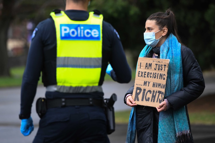 一名戴着口罩的妇女站在一个牌子上，上面写着 "我只是在行使......我的人权"。