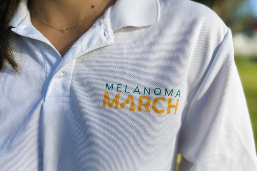 A woman with dark hair wearing long sleeved white sun safe shirt and close up of shirts emblem.