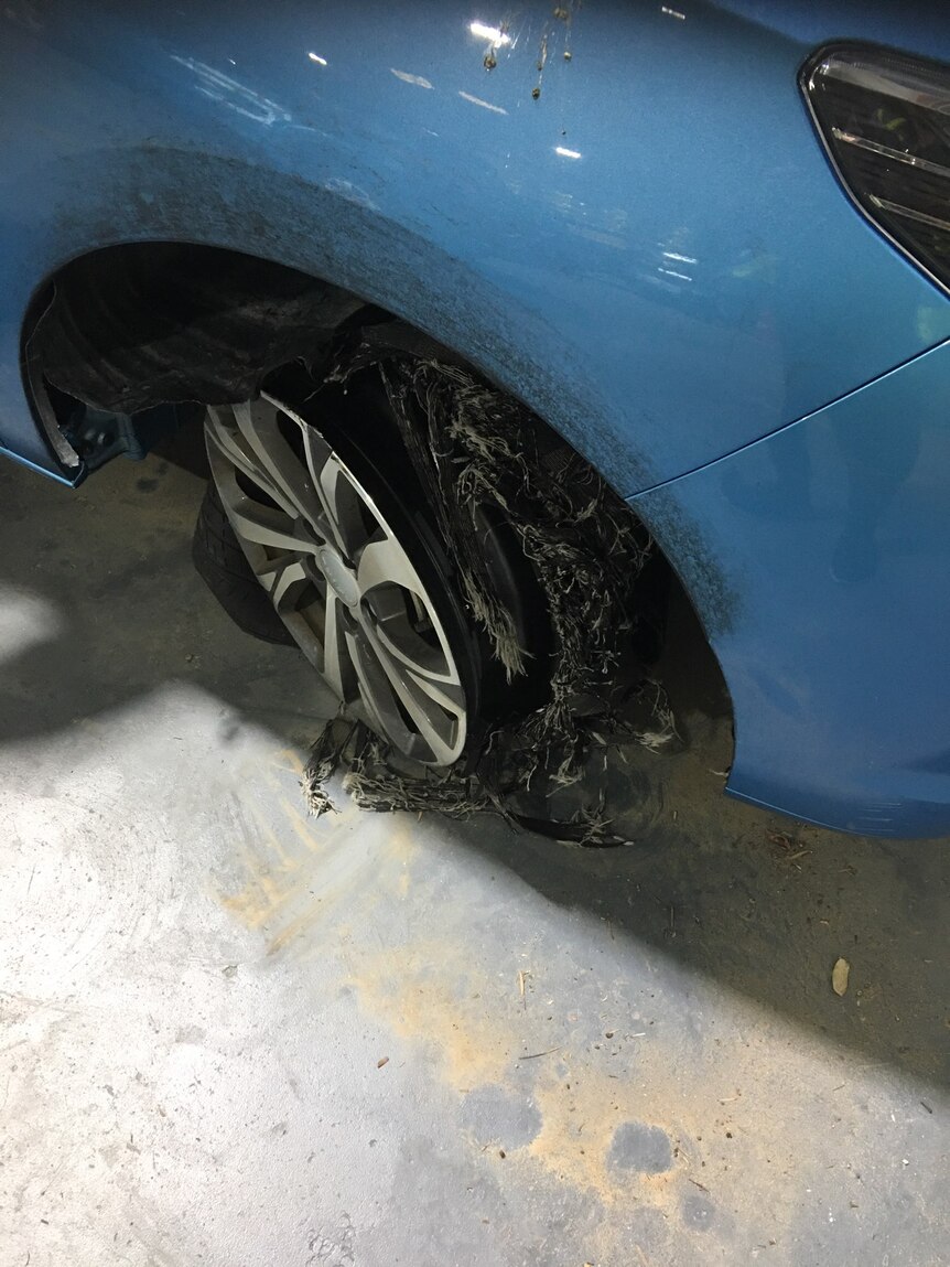 A shredded front tyre on a blue car. 