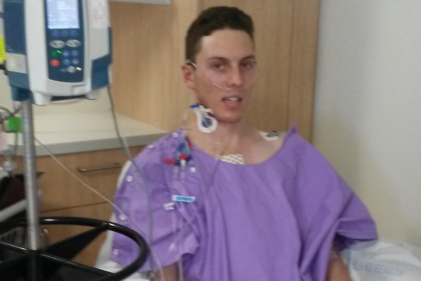 Lachlan Raso sits up in hospital with various tubes attached to him.