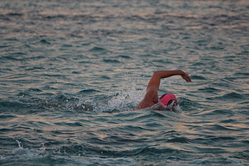 A man wearing a pink swimming cap swimming freestyle in the open ocean.