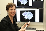  Professor Aileen McGonigal holding a smartwatch in front of a brain scan. 