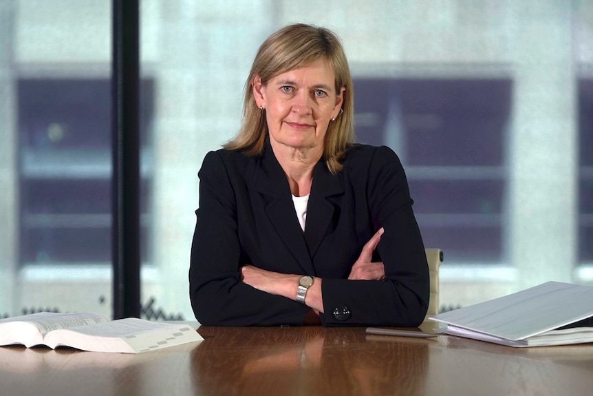 ASIC deputy chair Sarah Court is sitting at a desk with arms crossed looking directly at the camera