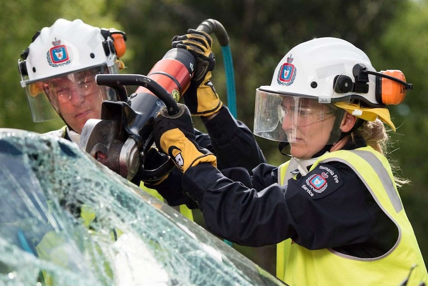Firefighter using powerful electric tool to cut open the windscreen of a car with another looking on.