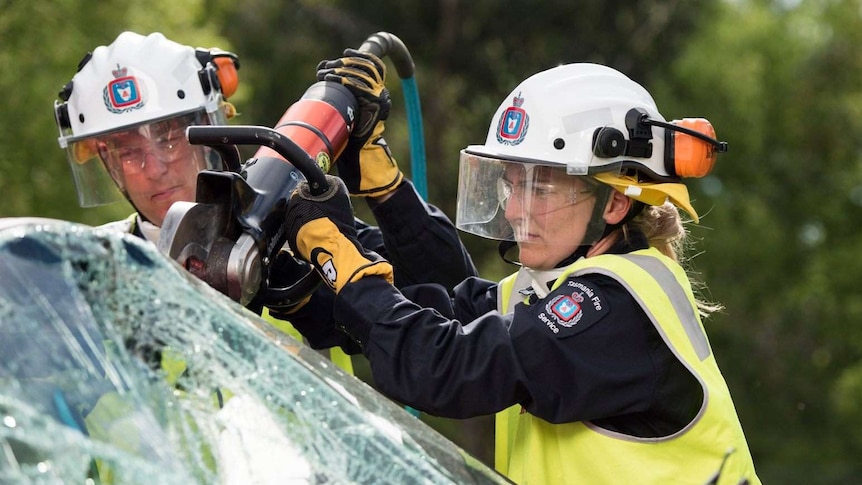 A firefighter using an electric tool to cut open the windscreen of a car.