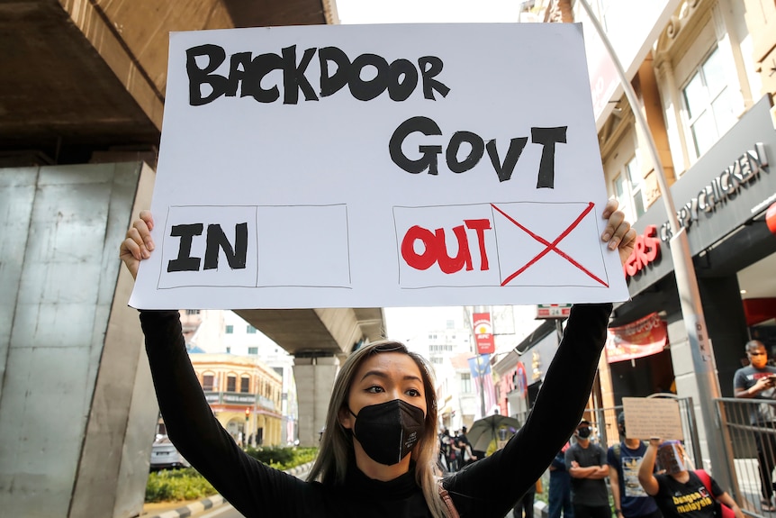 A protester holds a placard reading 'backdoor govt: out' at a protest demanding Malaysia's prime minister resign