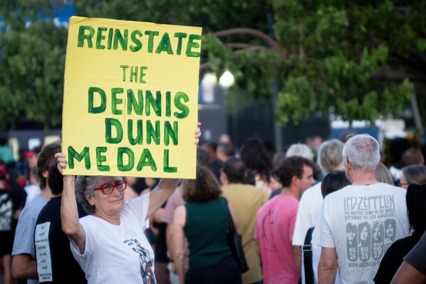 达尔文市一场 AFL 比赛外，为丹尼斯·邓恩 (Dennis Dunn) 进行抗议的人群，背景中观众在门口排队。