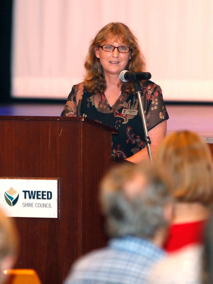 A woman stands behind a lectern, giving a talk.