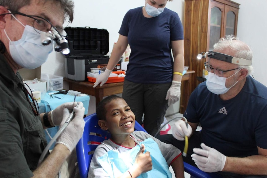 An East Timorese boy gives a thumbs up after dental care from Dr Malcolm Campbell, nurse Bec Apps and Dr Mark Tuffley.
