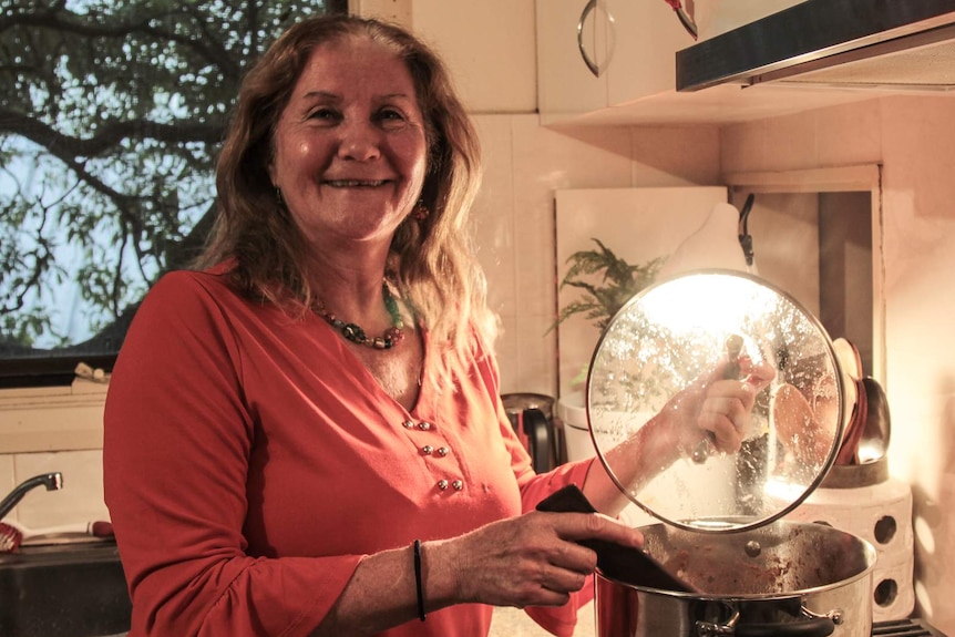 A woman holds a saucepan lid over her stove while a bright light shines through it. She's smiling for the camera.