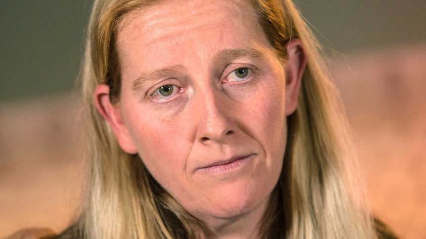 A headshot of a woman with long blond hair, wearing a black jacket.