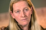 A headshot of a woman with long blond hair, wearing a black jacket.