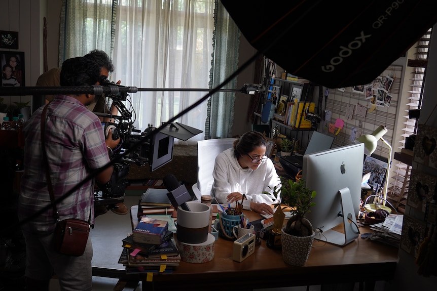 A woman sits at the computer on a movie set.