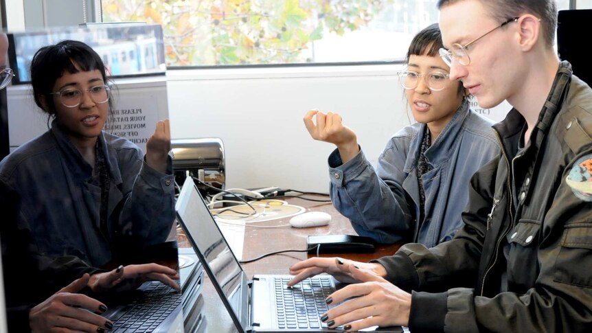 two people looking at a laptop computer, while one types