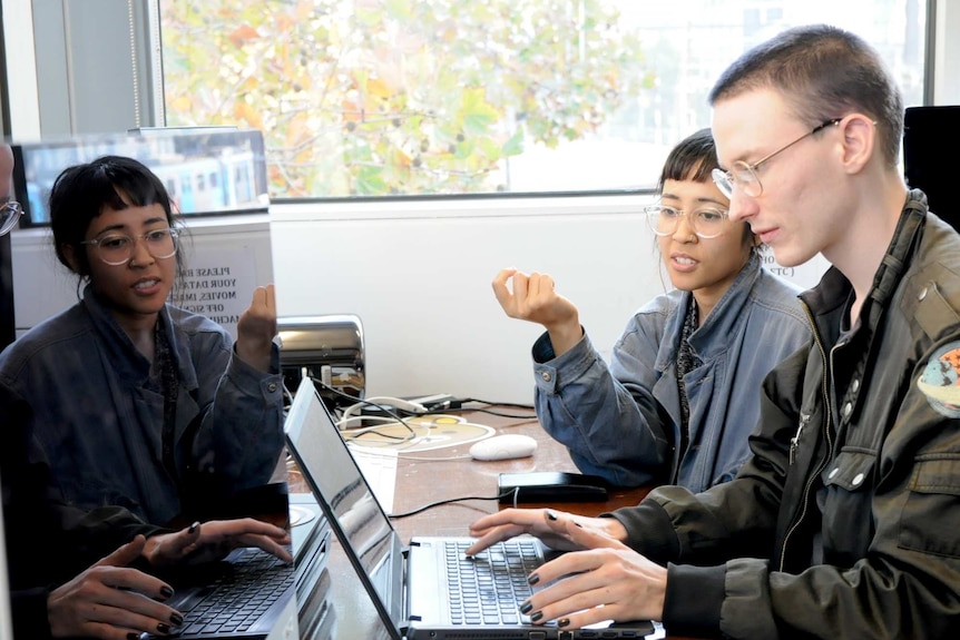 two people looking at a laptop computer, while one types