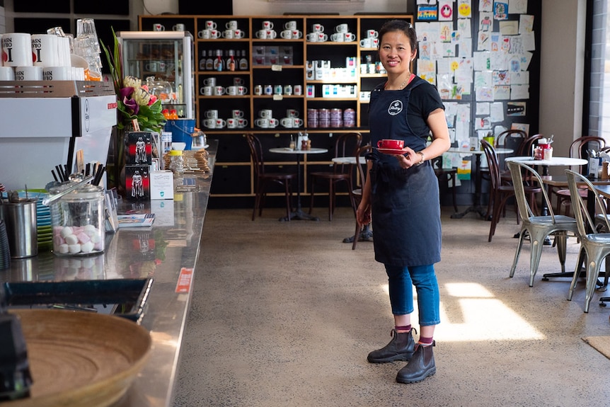 Ruby Gleeson holding a coffee cup while standing in a cafe venue to depict tips for people standing all day.
