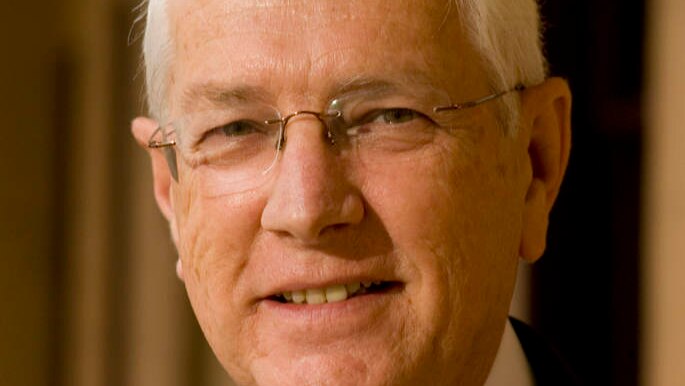 A portrait shot of a smiling man wearing glasses and a suit.