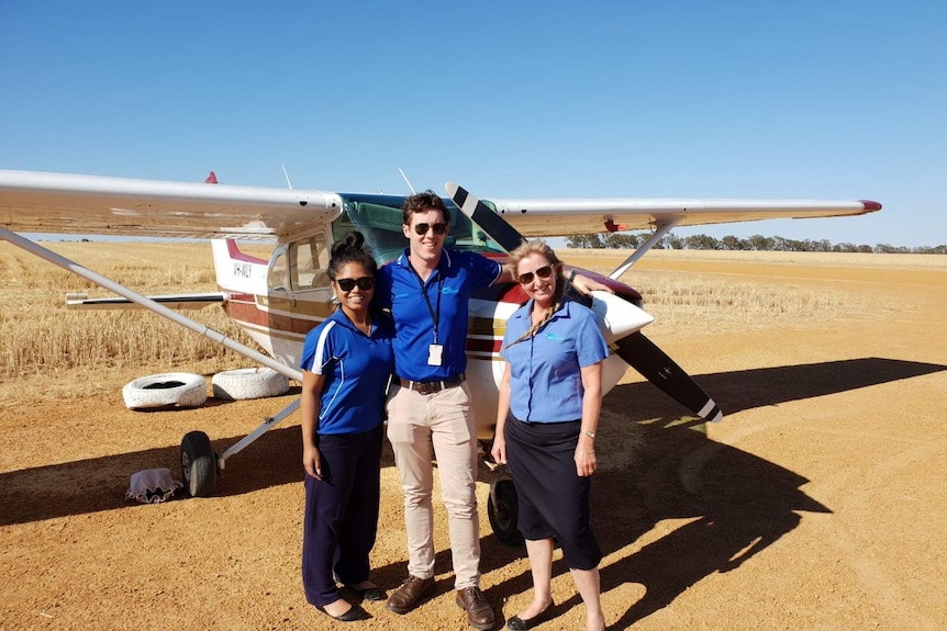 A man and two women stand next to a light aircraft in a wheat field in Western Australia.