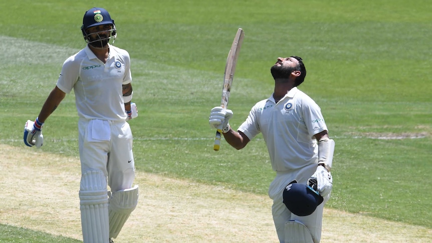 Cheteshwar Pujara looks skywards as he raises his bat after scoring a century while Virat Kohli looks on