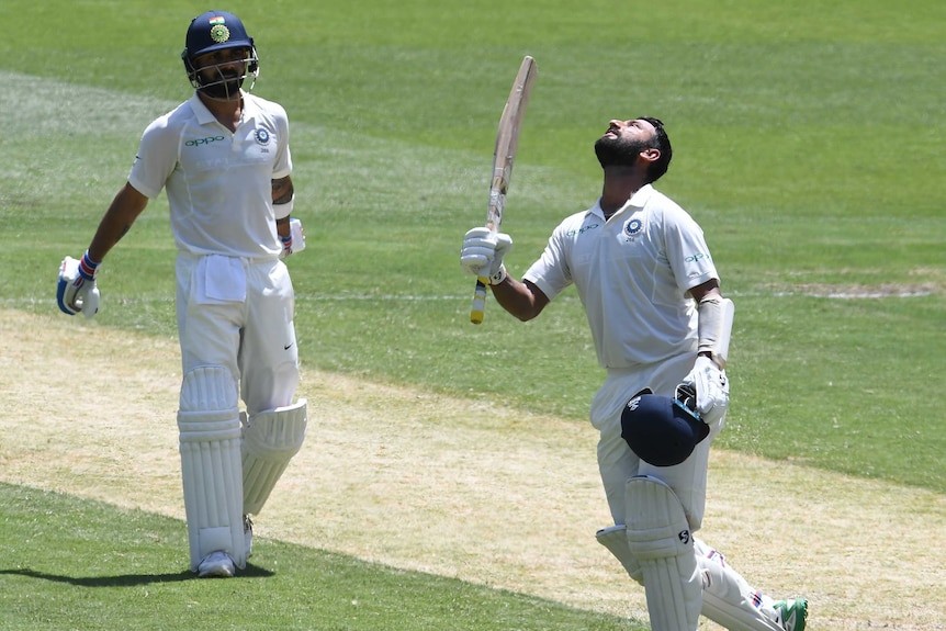 Cheteshwar Pujara looks skywards as he raises his bat after scoring a century while Virat Kohli looks on