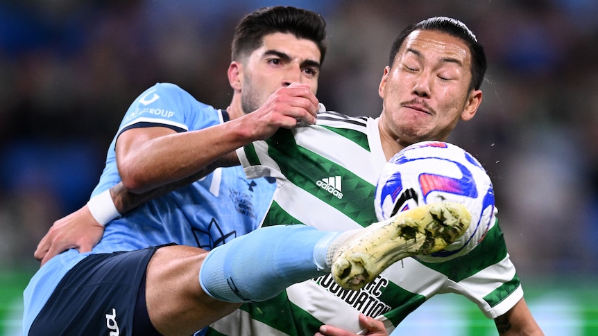 A Sydney FC A-League Men player challenges a Celtic opponent for the ball.