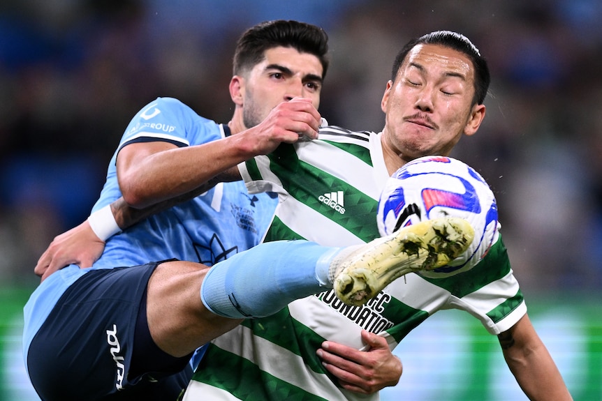 A Sydney FC A-League Men player challenges a Celtic opponent for the ball.