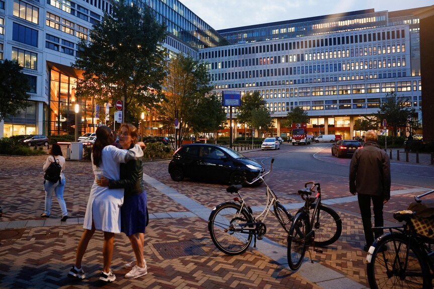 Two people are pictured hugging in front of the Erasmus Medical Center at dawn.