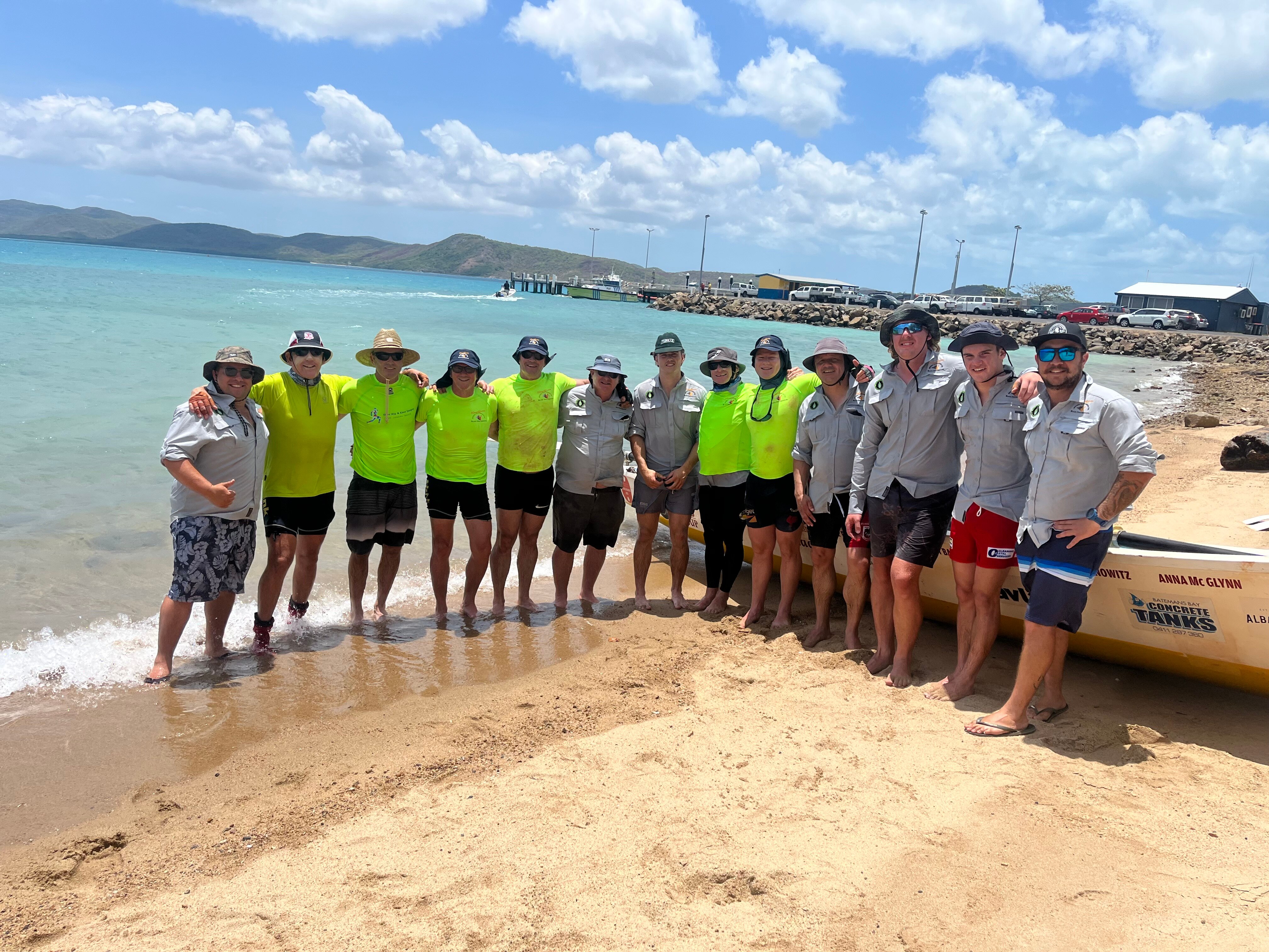 A group of men stand arm in arm on the beach.
