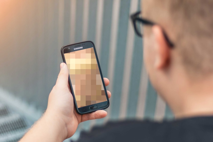 An unidentifiable man holds a phone. The image on it is pixelated