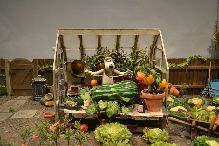 Gromit character measuring a watermelon in a garden