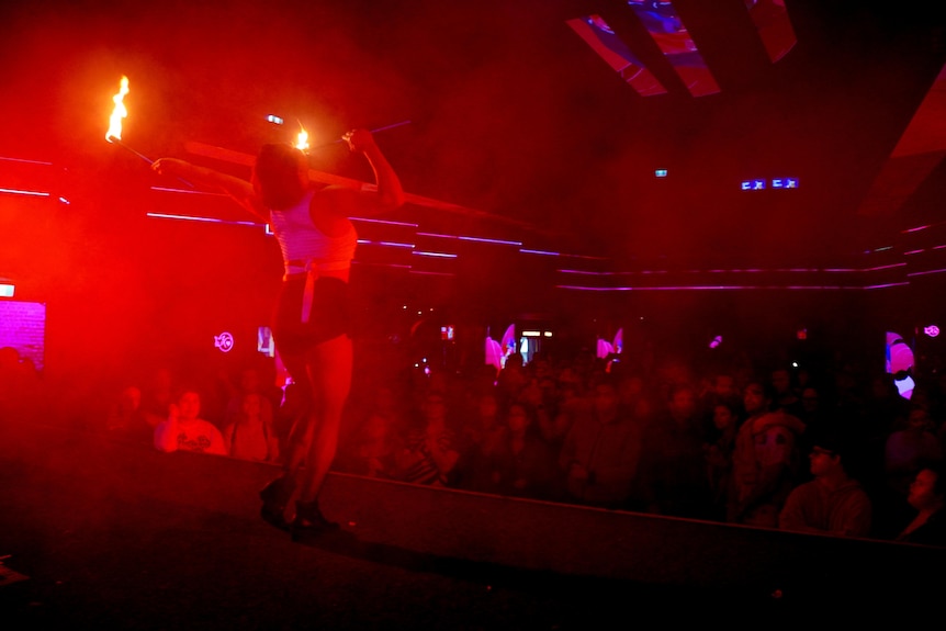 A dancer on a stage is watched by people as a red light shines from the left. 