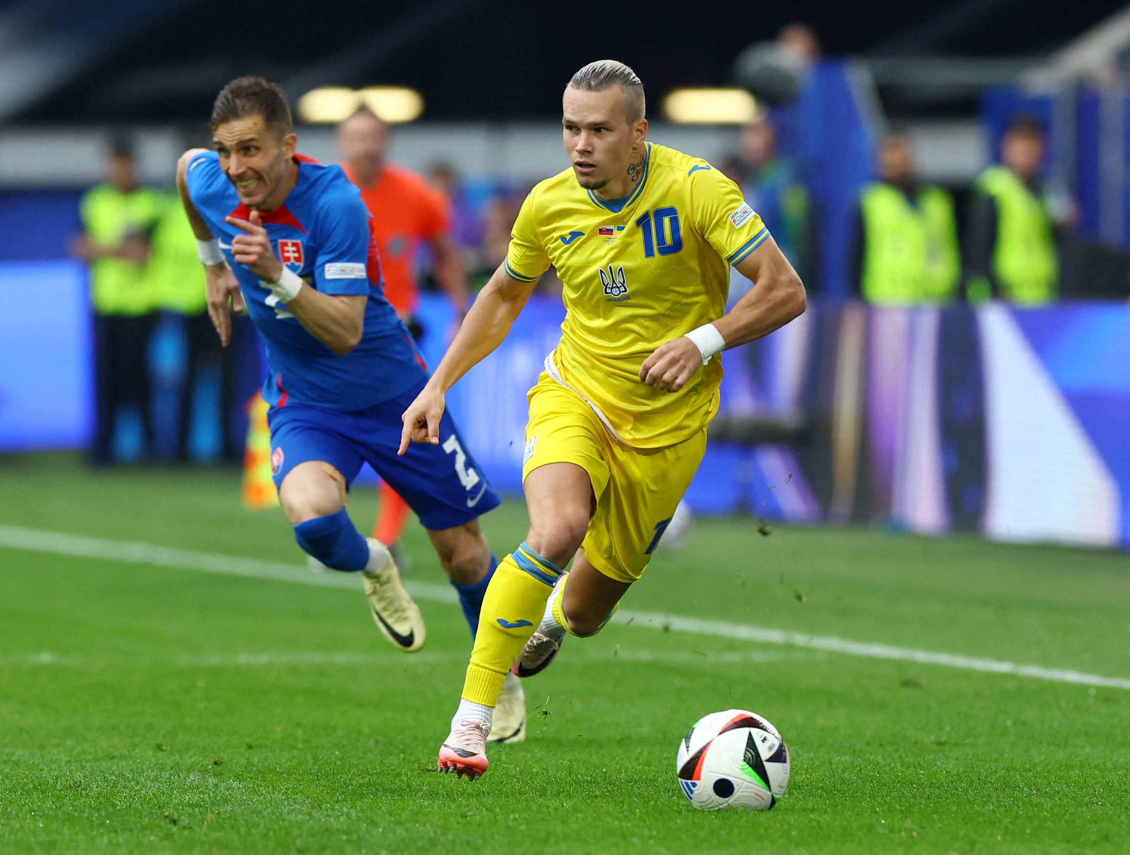 A young man in a bright yellow football kit runs down the pitch with the ball.