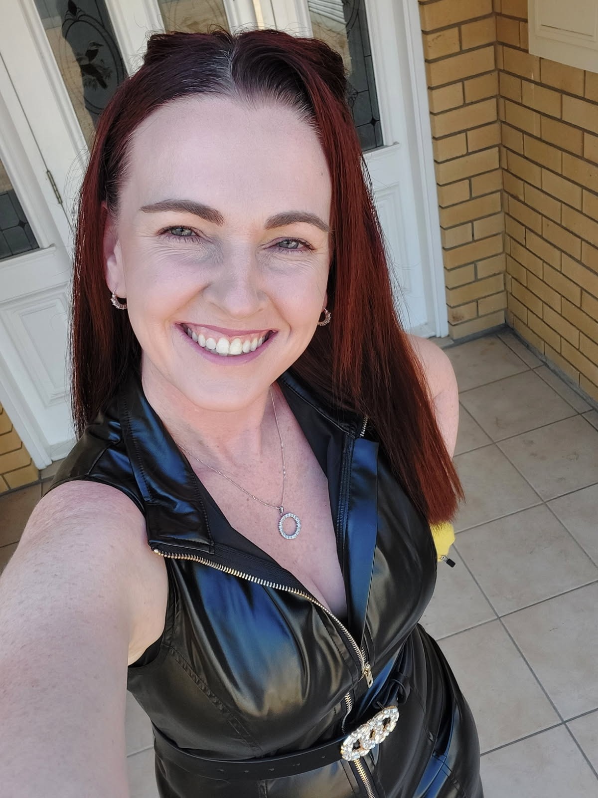 A woman with red hair smiling and wearing a leather dress