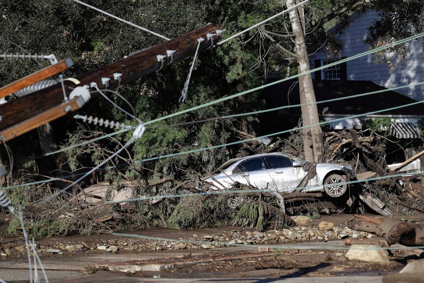 A damaged car sits over fallen and debris behind downed power lines