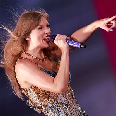 Taylor Swift, a singer with long blonde hair holds a microphone in one hand and points with the other