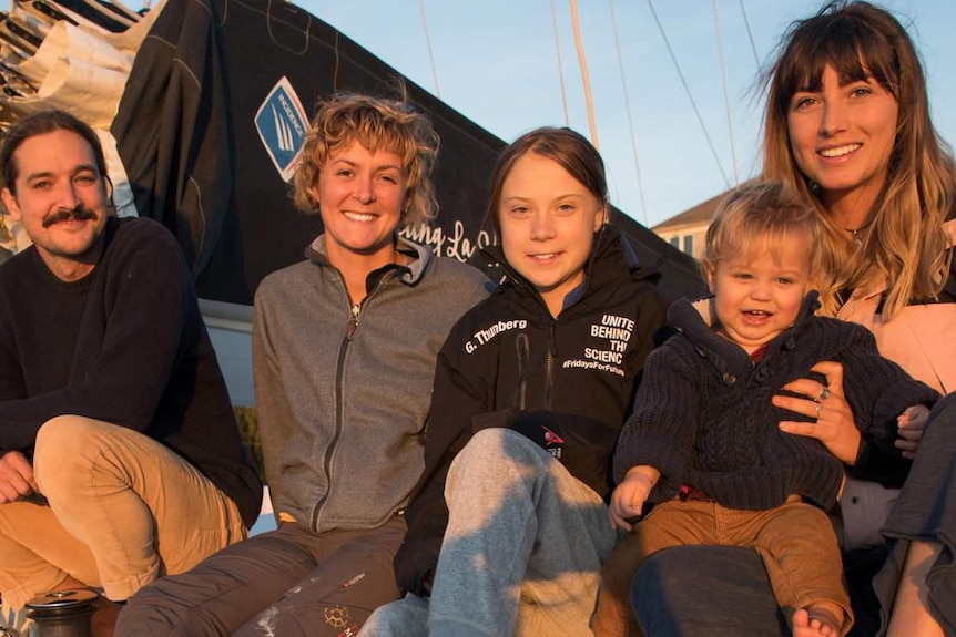 Four people and a baby sit on a yacht.