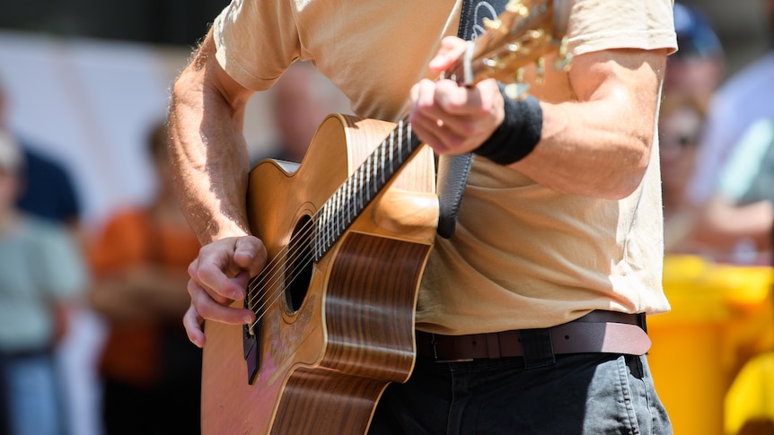 a close-up photo of a man playing an acoustic guitar, his head is cropped out of the frame